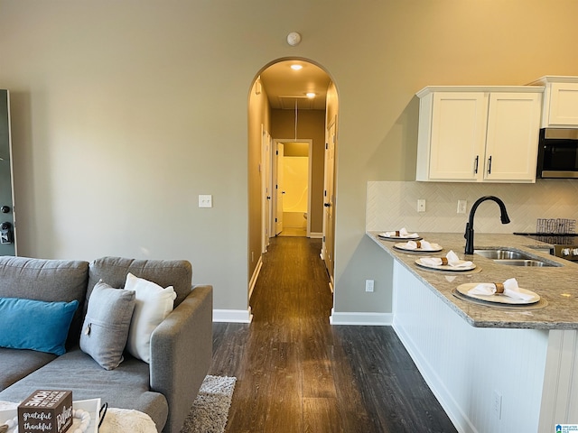 kitchen featuring arched walkways, a sink, white cabinets, open floor plan, and stainless steel microwave