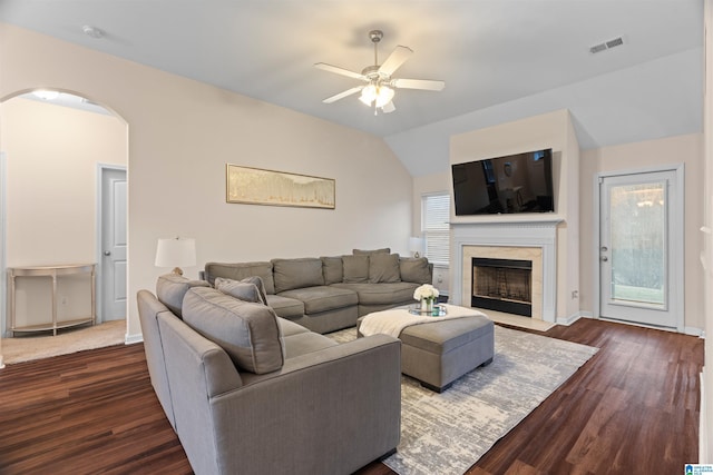 living area featuring dark wood finished floors, lofted ceiling, visible vents, a premium fireplace, and a ceiling fan