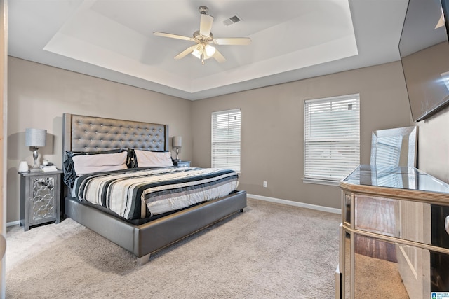 bedroom featuring baseboards, visible vents, a raised ceiling, light colored carpet, and ceiling fan