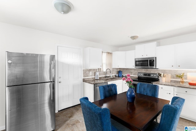 kitchen featuring stainless steel appliances, backsplash, white cabinetry, a sink, and dark stone counters