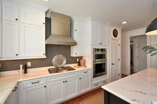 kitchen featuring wall chimney exhaust hood, light stone counters, stainless steel appliances, white cabinetry, and backsplash