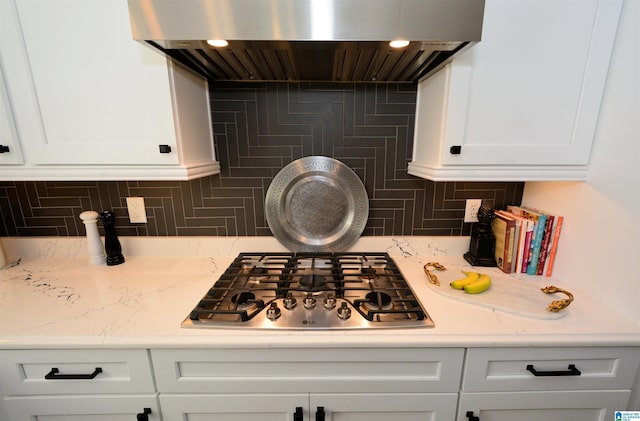 kitchen featuring wall chimney range hood, stainless steel gas stovetop, white cabinetry, and backsplash