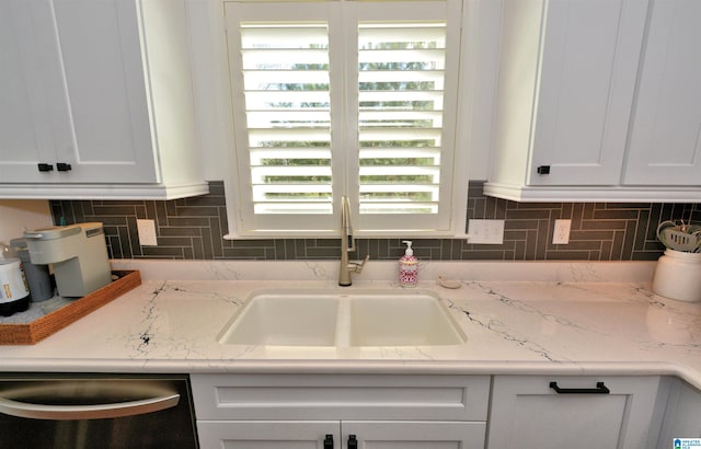 kitchen featuring light stone counters, backsplash, white cabinets, a sink, and dishwasher