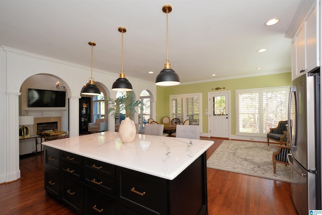 kitchen with dark wood-type flooring, open floor plan, dark cabinetry, freestanding refrigerator, and a glass covered fireplace