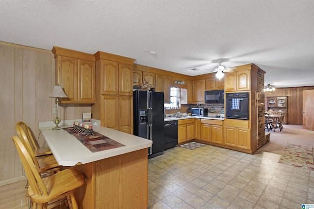 kitchen featuring light floors, a peninsula, light countertops, black appliances, and a kitchen bar