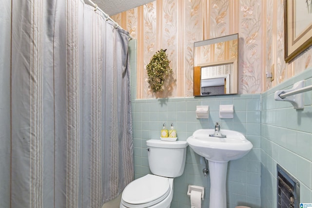 bathroom featuring a textured ceiling, toilet, tile walls, wainscoting, and wallpapered walls