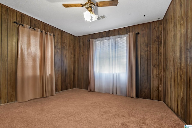 spare room with visible vents, carpet, a ceiling fan, and wooden walls