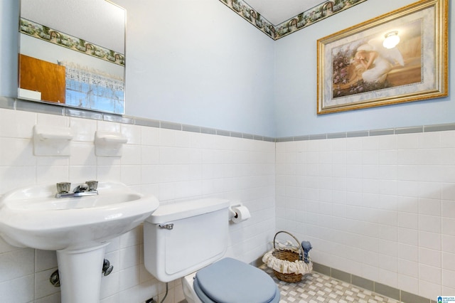 half bath featuring toilet, a wainscoted wall, and tile walls