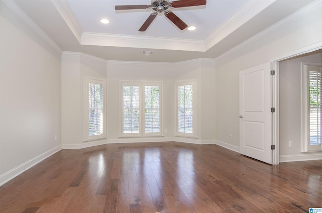 unfurnished room featuring a tray ceiling, dark wood-style flooring, crown molding, and baseboards