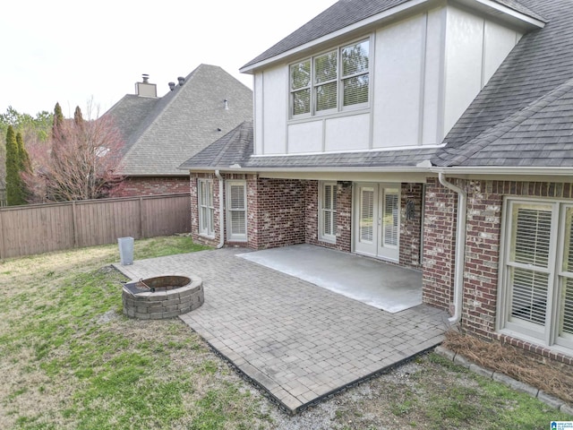 rear view of property with a fenced backyard, a fire pit, brick siding, stucco siding, and a patio area