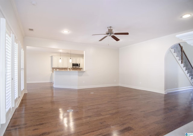 unfurnished living room with arched walkways, ornamental molding, stairway, and dark wood finished floors