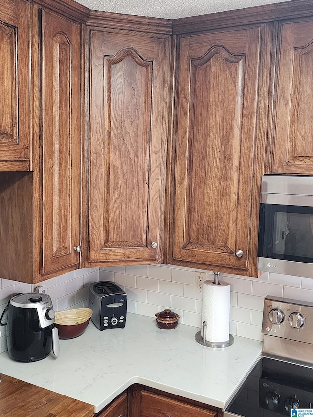 kitchen with appliances with stainless steel finishes, brown cabinets, and tasteful backsplash