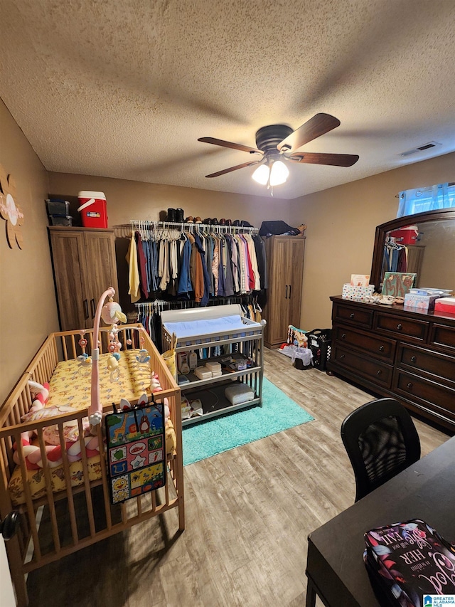 bedroom featuring light wood-type flooring, visible vents, ceiling fan, and a textured ceiling