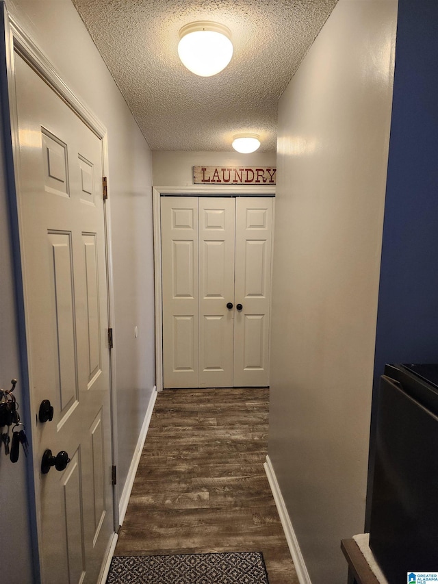 corridor with dark wood finished floors, a textured ceiling, and baseboards