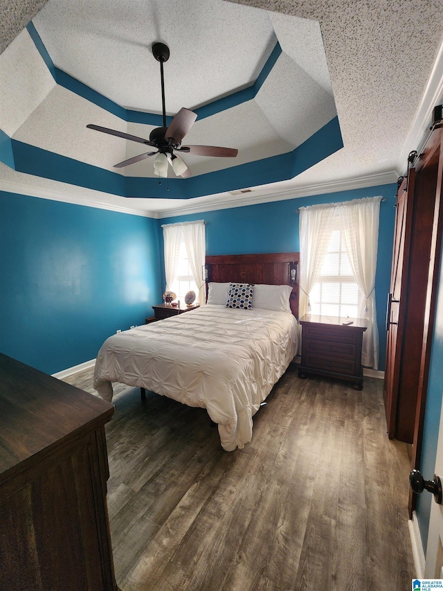 bedroom featuring dark wood-style flooring, crown molding, a raised ceiling, a barn door, and a textured ceiling