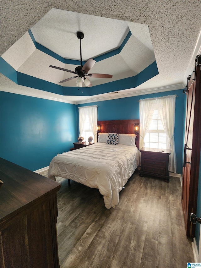 bedroom with dark wood-style floors, a raised ceiling, a barn door, ornamental molding, and a textured ceiling