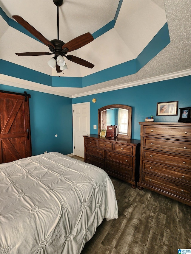 bedroom with ceiling fan, a barn door, dark wood-style flooring, a tray ceiling, and crown molding