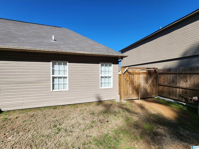 exterior space with roof with shingles, a lawn, fence, and a gate