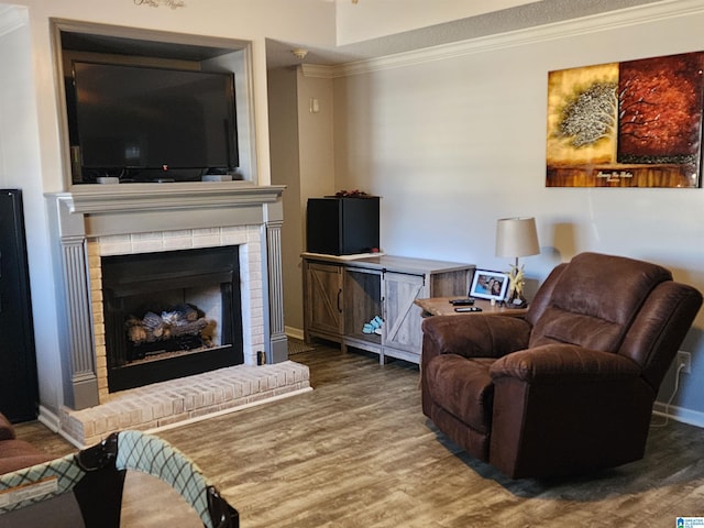 living room with a brick fireplace, crown molding, baseboards, and wood finished floors