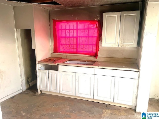 kitchen featuring unfinished concrete flooring, a sink, and white cabinets