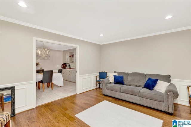 living room featuring light wood finished floors, ornamental molding, a wainscoted wall, and an inviting chandelier