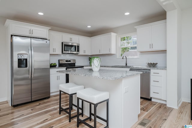 kitchen featuring stainless steel appliances, a kitchen island, visible vents, white cabinetry, and light stone countertops