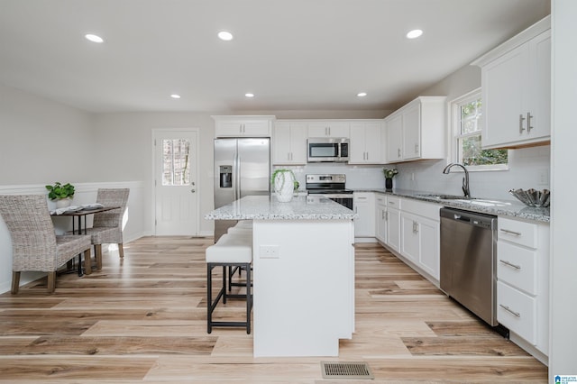 kitchen featuring stainless steel appliances, a kitchen island, visible vents, white cabinets, and light stone countertops