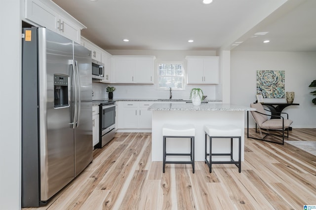 kitchen with appliances with stainless steel finishes, light wood-type flooring, a center island, and white cabinets