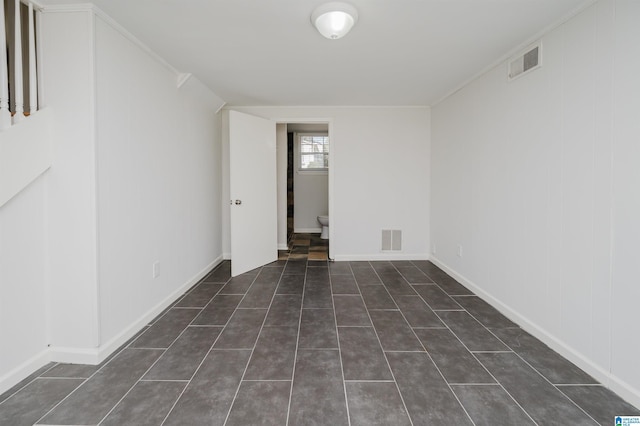 spare room with crown molding, dark tile patterned flooring, visible vents, and baseboards