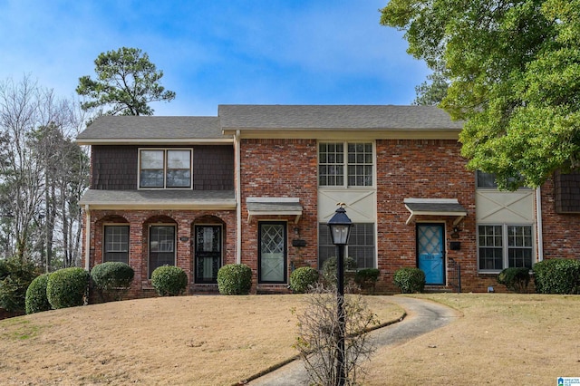 view of front of property featuring a shingled roof, brick siding, and a front lawn