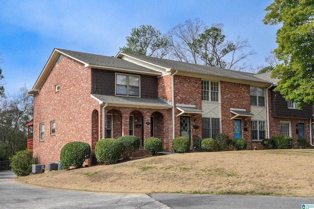 view of front facade with roof with shingles, cooling unit, and brick siding