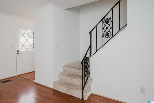 staircase featuring ornamental molding, visible vents, baseboards, and wood finished floors