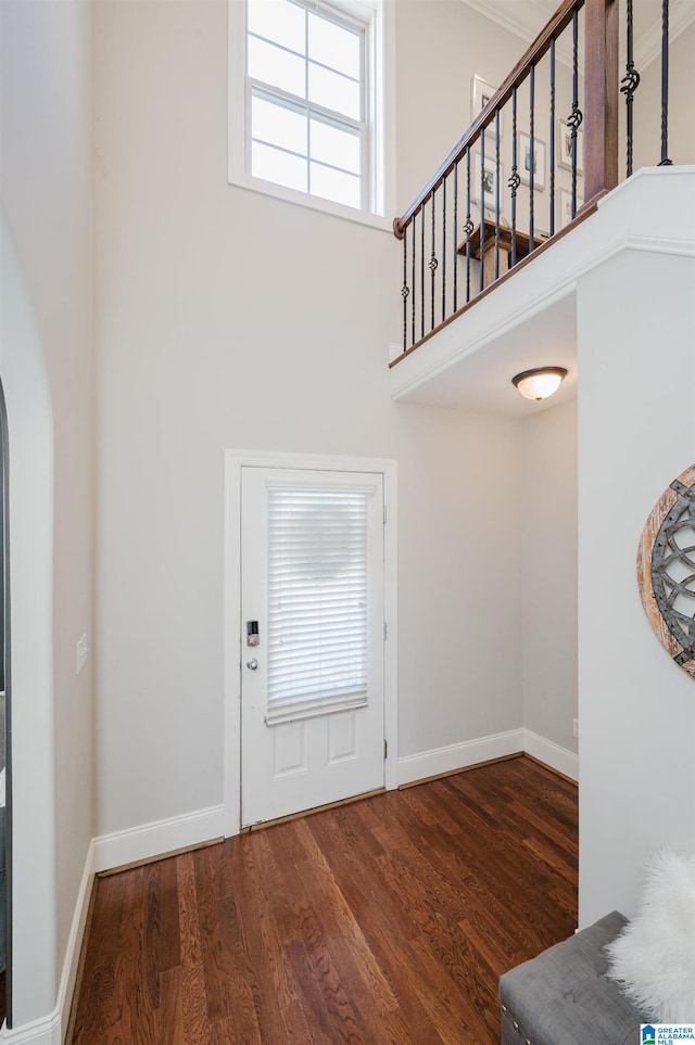 foyer entrance featuring arched walkways, wood finished floors, a towering ceiling, and baseboards