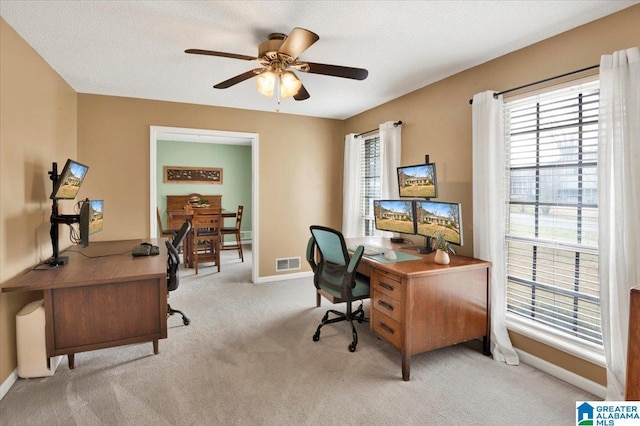 office space featuring light carpet, baseboards, visible vents, a ceiling fan, and a textured ceiling