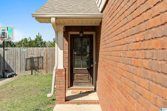 doorway to property with brick siding, roof with shingles, and fence