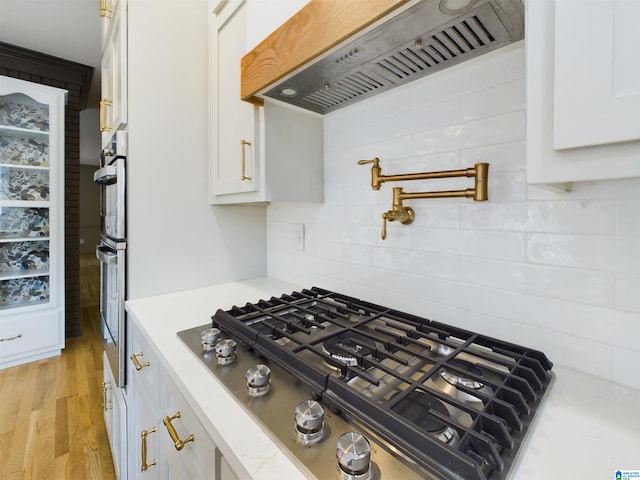 kitchen with custom range hood, appliances with stainless steel finishes, light countertops, light wood-type flooring, and white cabinetry