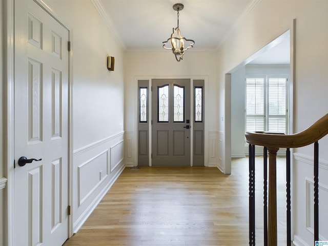 entrance foyer with a notable chandelier, crown molding, a decorative wall, light wood-style flooring, and stairs