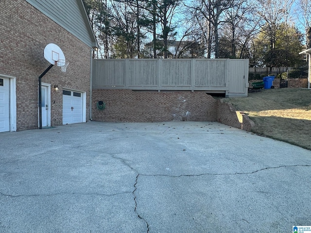 view of side of property featuring driveway, fence, and brick siding