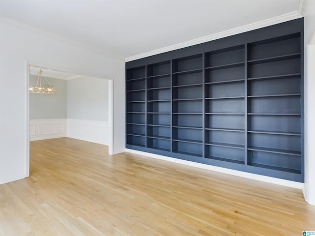 unfurnished room with light wood finished floors, built in features, a wainscoted wall, ornamental molding, and an inviting chandelier