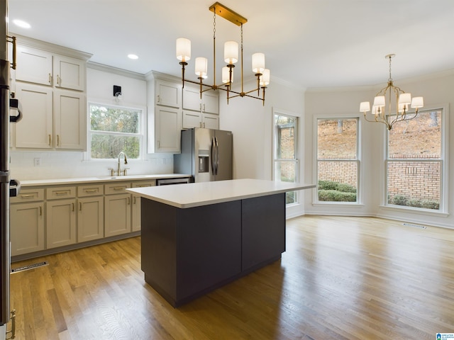 kitchen featuring a sink, light countertops, ornamental molding, stainless steel refrigerator with ice dispenser, and an inviting chandelier