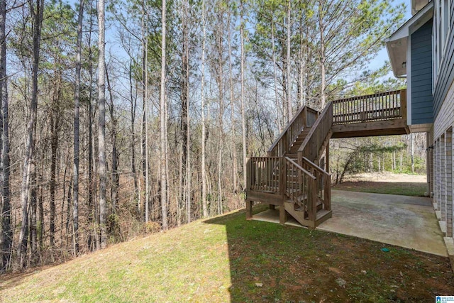 view of yard featuring a deck, a patio, stairway, and a forest view