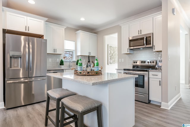 kitchen featuring stainless steel appliances, a kitchen island, white cabinets, light wood-type flooring, and a kitchen bar