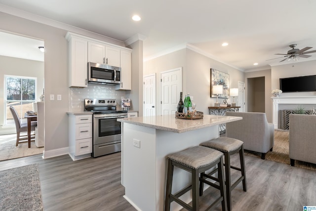 kitchen featuring tasteful backsplash, appliances with stainless steel finishes, dark wood-type flooring, white cabinetry, and a kitchen bar