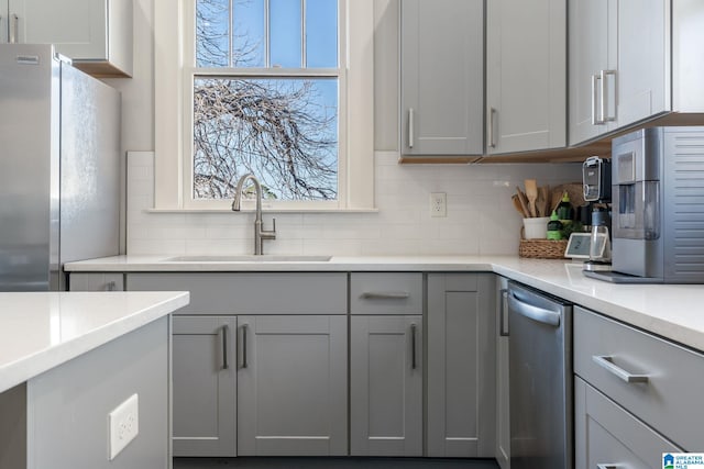 kitchen featuring gray cabinets, light countertops, backsplash, freestanding refrigerator, and a sink