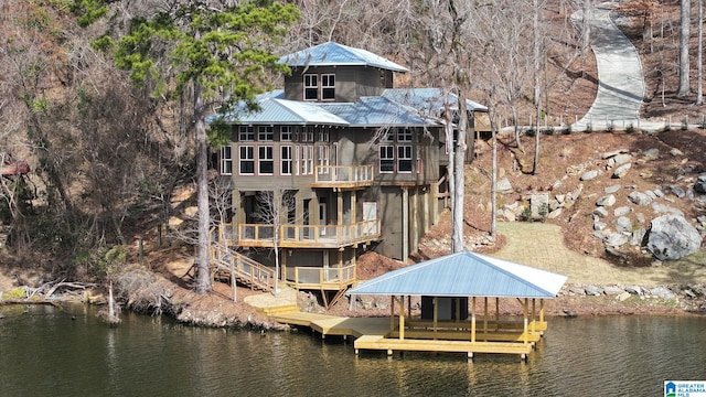 rear view of house with metal roof, a water view, boat lift, and a balcony