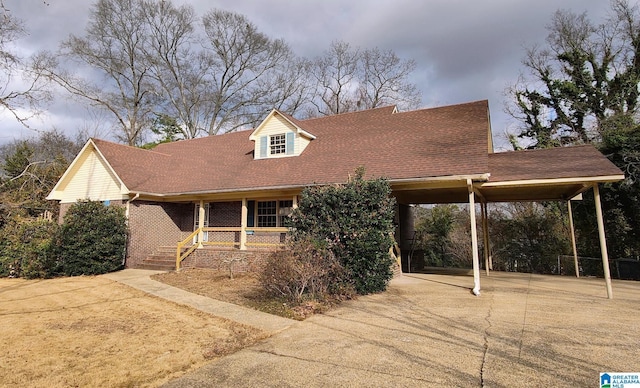 cape cod house featuring a shingled roof, concrete driveway, brick siding, and covered porch