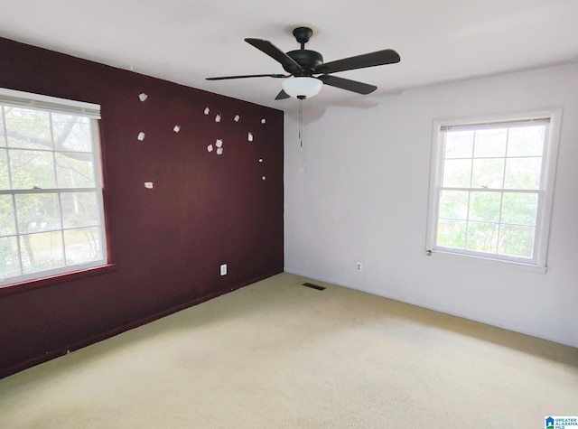 spare room featuring light carpet, ceiling fan, visible vents, and a wealth of natural light