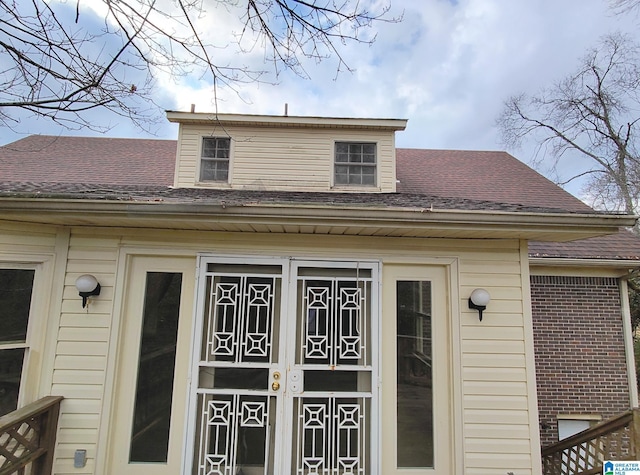 view of exterior entry with brick siding and roof with shingles