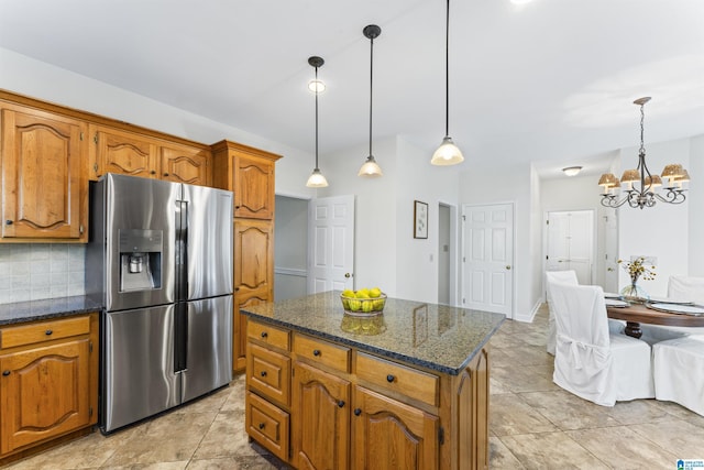 kitchen with decorative backsplash, brown cabinets, dark stone counters, stainless steel fridge, and decorative light fixtures