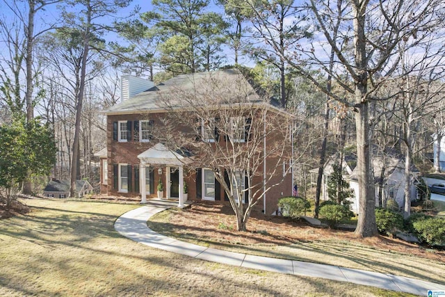 view of front of home with a front lawn, a chimney, and brick siding